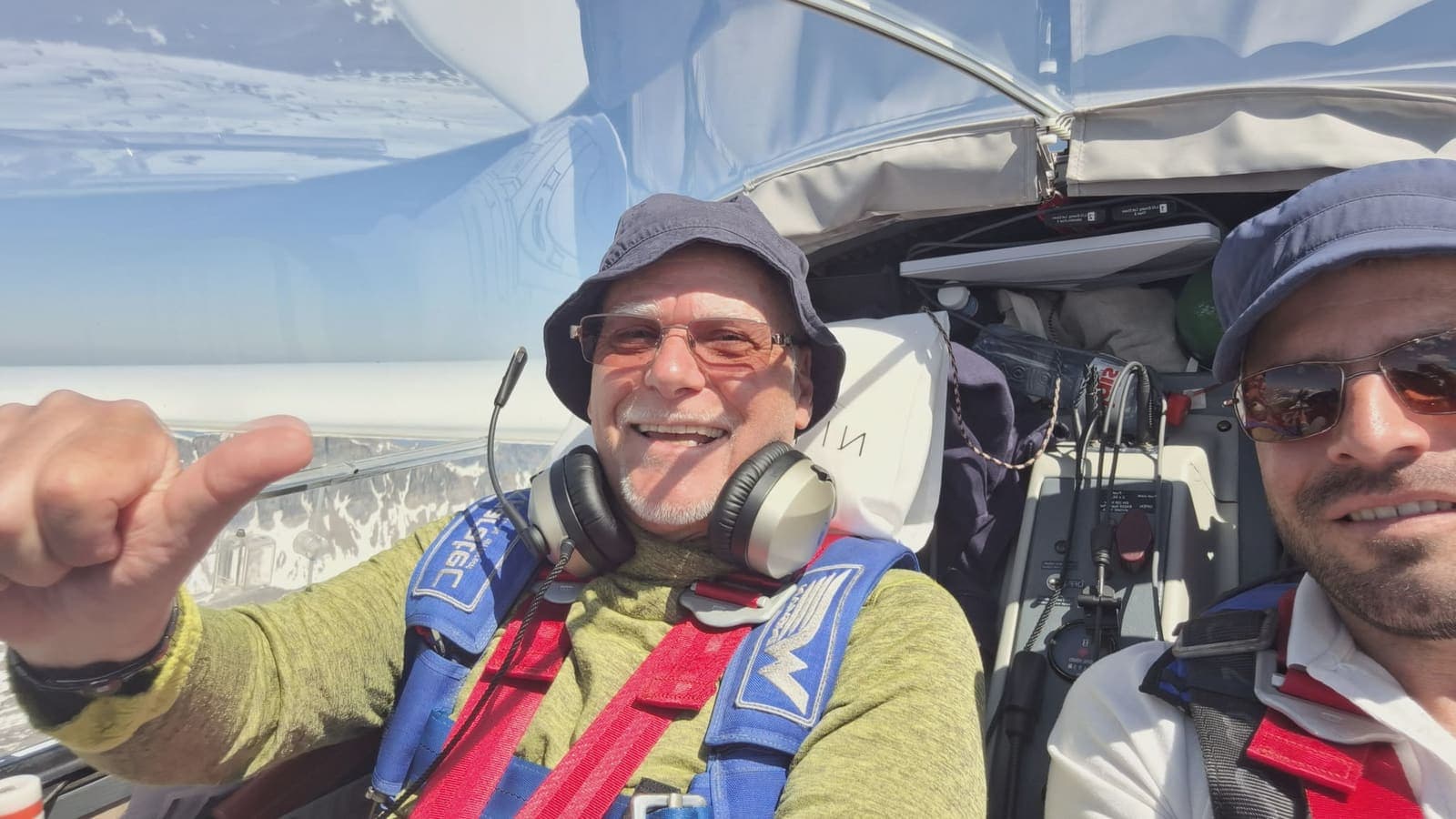 Ein begeisterter Passagier zeigt den Daumen hoch neben dem Piloten hoch über den verschneiten Alpen