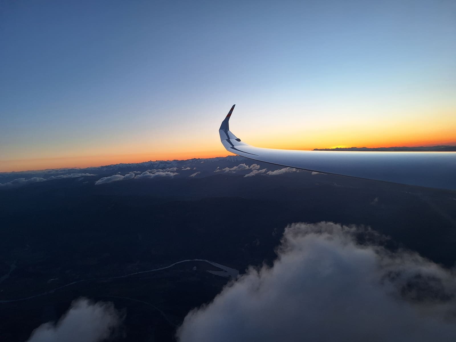 Sunrise over a dark mountain ridge seen past the glider wing during the dawn wave climb