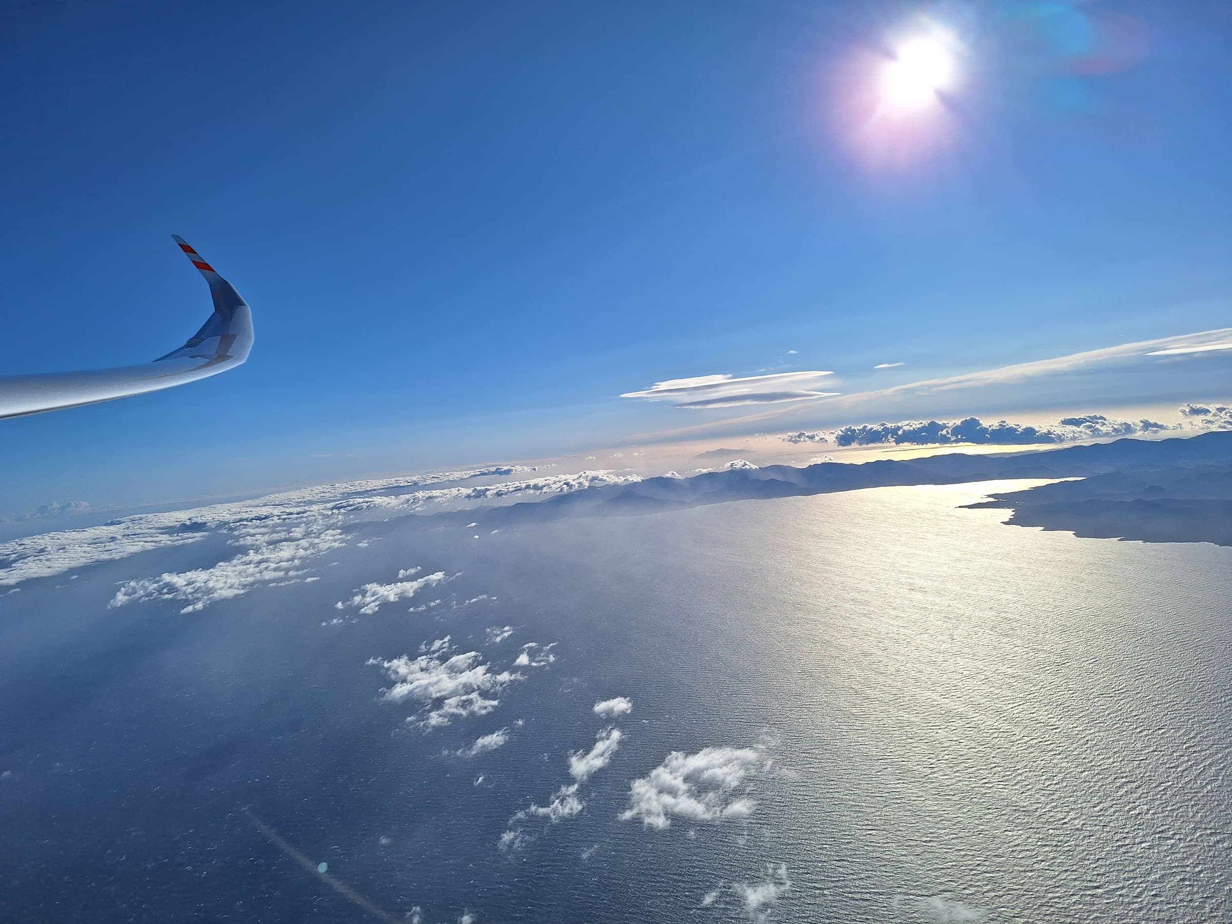 Glider wing over the Mediterranean, sunlight glittering on the open sea between France and Corsica